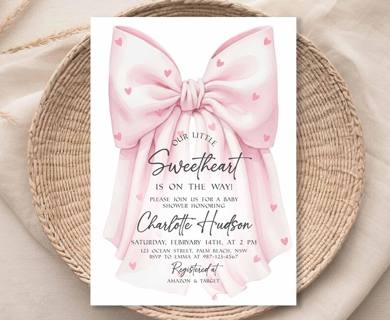 May include: A baby shower invitation featuring a large pink bow adorned with small pink hearts. The text reads "Our Little Sweetheart Is On The Way!" and includes details for Charlotte Hudson's baby shower, including date, time, and location.