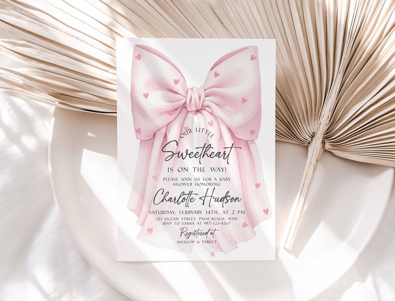 May include: A baby shower invitation featuring a large pink bow adorned with small pink hearts. The text "Our Little Sweetheart Is On The Way!" is displayed, along with the honoree's name, date, time, and RSVP information.