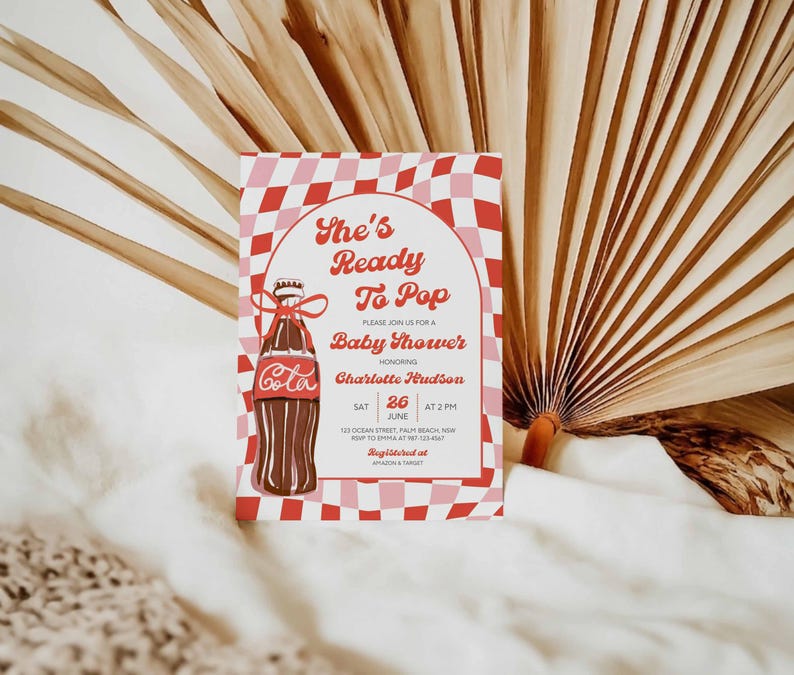 May include: A baby shower invitation with a retro design. The invitation features a Coca-Cola bottle illustration and the text "She's Ready To Pop." The background has a red and pink checkered pattern. The invitation includes the date, time, and location.