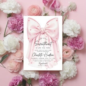 May include: A baby shower invitation with a large pink bow design and the text "Our Little Sweetheart is on the way!" surrounded by pink and white flowers. The invitation includes details for the baby shower honoring Charlotte Hudson.