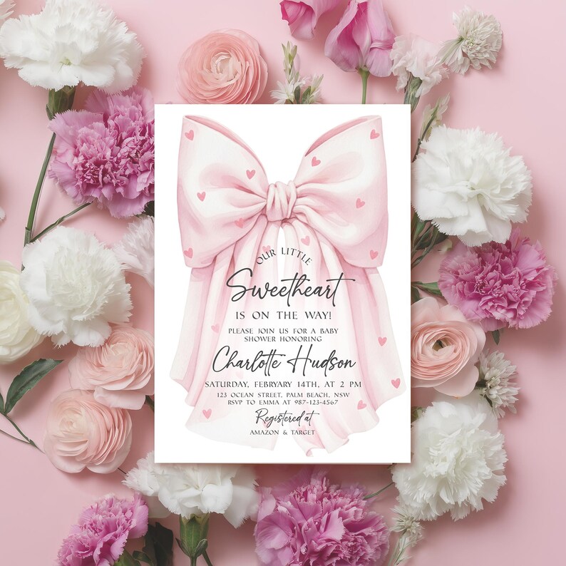 May include: A baby shower invitation with a large pink bow design and the text "Our Little Sweetheart is on the way!" surrounded by pink and white flowers. The invitation includes details for the baby shower honoring Charlotte Hudson.