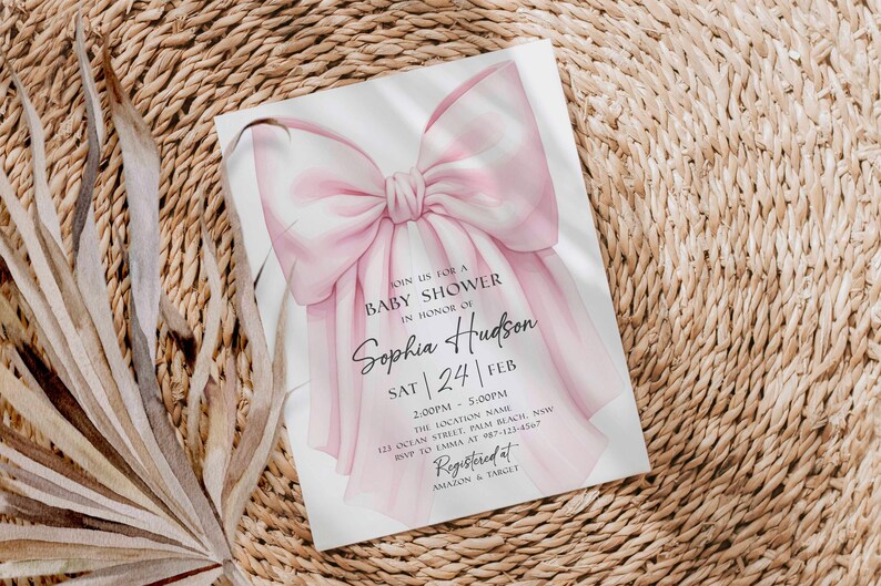 Op de afbeelding: Een uitnodiging voor een babyshower met een grote, aquarel roze strik. De uitnodiging bevat de tekst "Doe met ons mee voor een babyshower ter ere van Sophia Hudson" met evenementdetails. De uitnodiging staat op een geweven achtergrond.