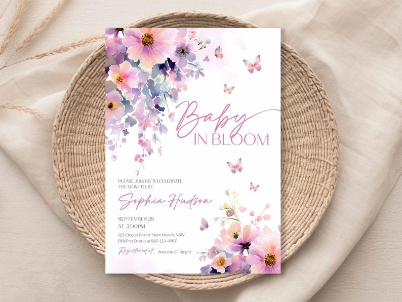 Może przedstawiać: Zaproszenie na baby shower z kwiatowym wzorem w odcieniach r&oacute;żu i fioletu, z napisem "Baby in Bloom". Zaproszenie zawiera szczeg&oacute;ły wydarzenia, takie jak data, godzina i miejsce.