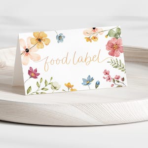 Può includere: Un biglietto bianco con un disegno floreale e il testo "food label" in un colore arancione pesca. I fiori sono in tonalità di rosa, giallo, blu e verde.