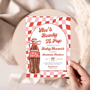 May include: Baby shower invitation with a retro design. The invitation features a brown soda bottle illustration with the word "Cola" and the text "She's Ready To Pop". The invitation is decorated with a red and pink checkered pattern.