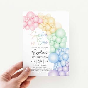May include: A birthday invitation with a rainbow balloon arch design. The invitation reads "Sophia is One" and includes details for a first birthday celebration, including the date, time, and location.