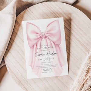 Op de afbeelding: Een uitnodiging voor een babyshower met een grote, zachtroze strik. De uitnodiging bevat de tekst "Baby Shower ter ere van Sophia Hudson" met de datum, tijd en locatiegegevens. De uitnodiging heeft een witte achtergrond.