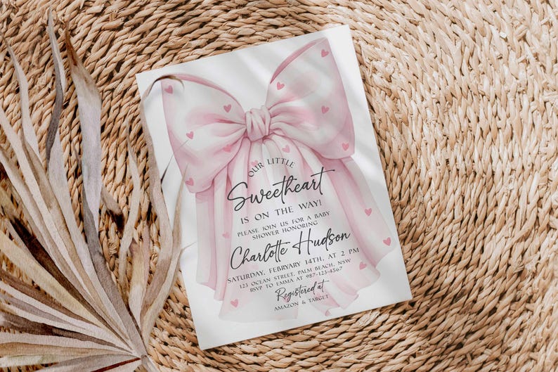 May include: Baby shower invitation with a watercolor bow design in shades of pink. The invitation includes the text "Our Little Sweetheart is on the way!" and details for the event, including the name Charlotte Hudson.
