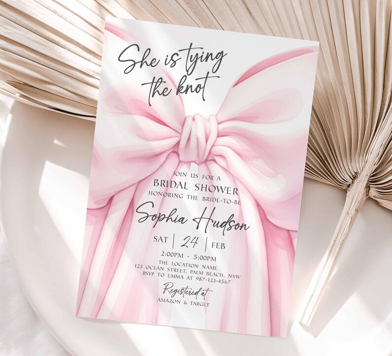 K&ouml;nnte beinhalten: Eine Einladung zur Brautparty mit einem gro&szlig;en rosa Schleifendesign und dem Text "She is tying the knot". Die Einladung enth&auml;lt Details f&uuml;r Sophia Hudsons Brautparty, einschlie&szlig;lich Datum, Uhrzeit und Ort. Registriert bei Amazon & Target.