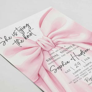 K&ouml;nnte beinhalten: Einladungskarte zur Brautparty mit gro&szlig;em rosa Schleifendesign. Die Einladung enth&auml;lt den Text &bdquo;She is tying the knot&ldquo; sowie Details f&uuml;r Sophia Hudsons Brautparty, einschlie&szlig;lich Datum, Uhrzeit und Ort.