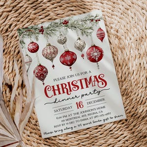 May include: A white Christmas dinner party invitation with red and green ornaments and a pine branch. The text reads "Please join us for a Christmas dinner party, Saturday 16 December, 6:00 PM at the Johnson's Home, 251 Montreal Ave, Regina CA, RSVP by Dec to Emma at 987-123-4567, Please bring along a 10$ secret Santa gift to share."