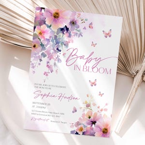 Może przedstawiać: Zaproszenie na baby shower z kwiatowym wzorem w odcieniach r&oacute;żu, fioletu i bieli. Zaproszenie zawiera napis "Baby in Bloom" w kursywie, wraz ze szczeg&oacute;łami wydarzenia, w tym imieniem "Sophia Hudson". Motyle są rozrzucone po całym projekcie.