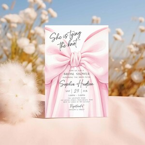 K&ouml;nnte beinhalten: Eine rechteckige Einladungskarte mit einer Illustration einer gro&szlig;en rosa Schleife. Der Text "She is tying the knot" steht oben, mit Details f&uuml;r eine Brautparty f&uuml;r Sophia Hudson, einschlie&szlig;lich Datum, Uhrzeit und Ort. Die Karte ist bei Amazon & Target registriert.