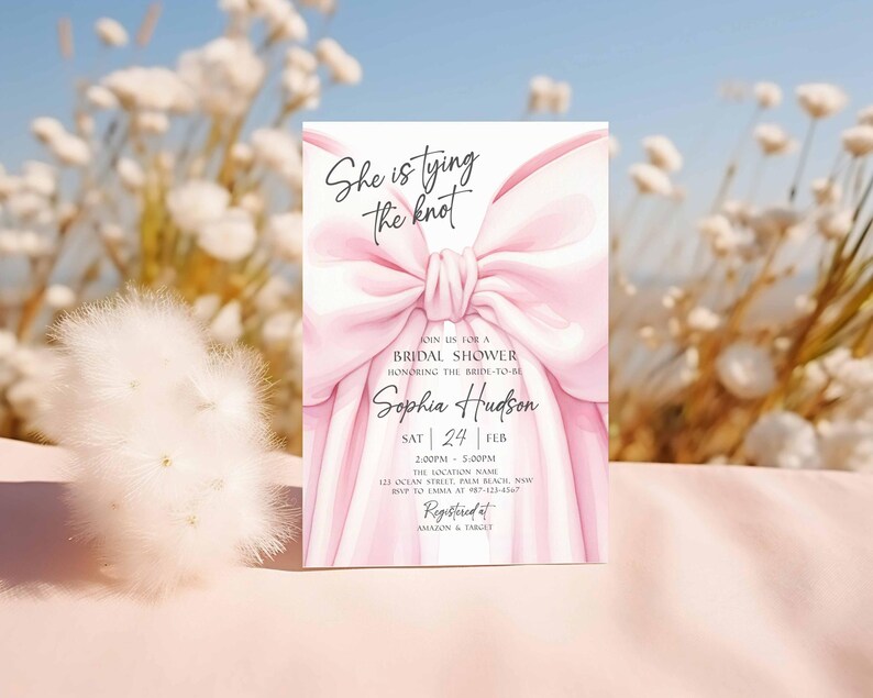 K&ouml;nnte beinhalten: Eine rechteckige Einladungskarte mit einer Illustration einer gro&szlig;en rosa Schleife. Der Text "She is tying the knot" steht oben, mit Details f&uuml;r eine Brautparty f&uuml;r Sophia Hudson, einschlie&szlig;lich Datum, Uhrzeit und Ort. Die Karte ist bei Amazon & Target registriert.