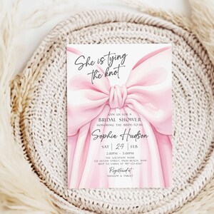 K&ouml;nnte beinhalten: Eine Einladung zur Brautparty mit einem gro&szlig;en rosa Schleifendesign. Der Text "She is tying the knot" steht oben, mit Details zur Veranstaltung darunter, einschlie&szlig;lich des Namens der Braut, Datum und Uhrzeit. Die Einladung befindet sich vor einem neutralen Hintergrund.