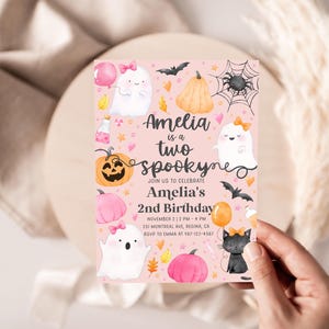 May include: A pink Halloween-themed invitation with the text "Amelia is a two spooky" and illustrations of ghosts, pumpkins, bats, and a black cat. The invitation is for Amelia's 2nd birthday.