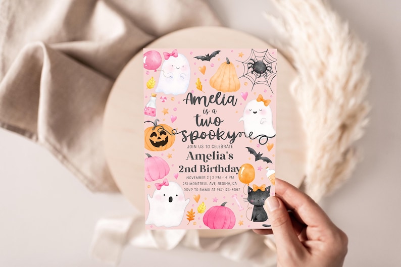 May include: A pink Halloween-themed invitation with the text "Amelia is a two spooky" and illustrations of ghosts, pumpkins, bats, and a black cat. The invitation is for Amelia's 2nd birthday.