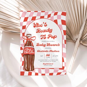 May include: A baby shower invitation with a retro design. The invitation features a brown cola bottle with a red bow, set against a red and pink checkered background. Text includes "She's Ready To Pop" and baby shower details.