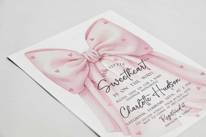 May include: A baby shower invitation featuring a large pink bow with small heart accents. The text reads "Our Little Sweetheart is on the way!" and includes details for the event, including the name "Charlotte Hudson".