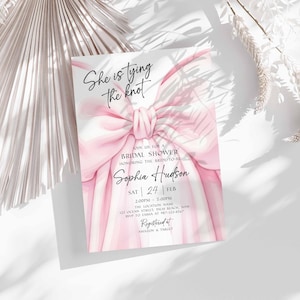 K&ouml;nnte beinhalten: Einladungskarte zur Brautparty mit rosa Schleife und dem Text "She is tying the knot". Die Einladung enth&auml;lt den Namen der Braut, Datum und Uhrzeit. Registriert bei Amazon & Target.