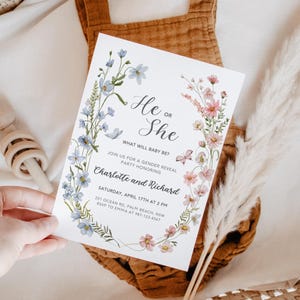 May include: A gender reveal party invitation with a floral wreath design in shades of blue and pink. The text reads "He or She? What will baby be? Join us for a gender reveal party honoring Charlotte and Richard. Saturday, April 17th at 2 PM. 251 Ocean Rd, Palm Beach, NSW. RSVP to Emma at 987-123-4567."