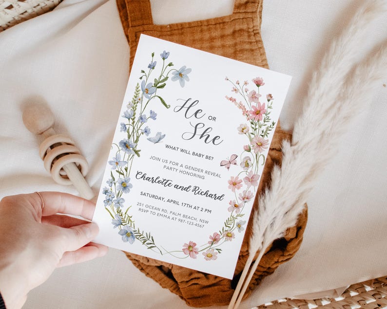 May include: A gender reveal party invitation with a floral wreath design in shades of blue and pink. The text reads "He or She? What will baby be? Join us for a gender reveal party honoring Charlotte and Richard. Saturday, April 17th at 2 PM. 251 Ocean Rd, Palm Beach, NSW. RSVP to Emma at 987-123-4567."