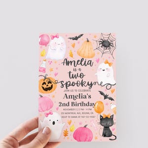 May include: A pink Halloween-themed birthday invitation with the text "Amelia is a two spooky" and event details. The design includes ghosts, pumpkins, bats, and a black cat. The invitation is held by a hand.