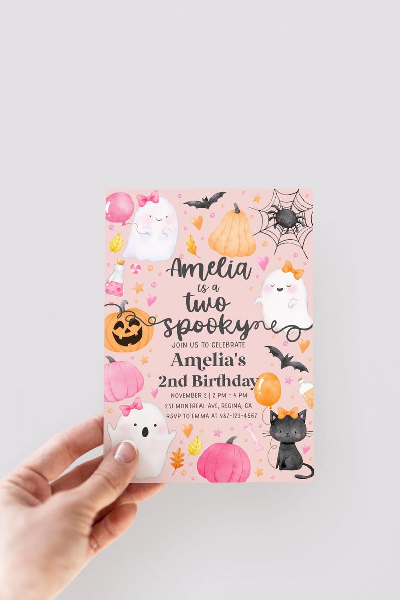 May include: A pink Halloween-themed birthday invitation with the text "Amelia is a two spooky" and event details. The design includes ghosts, pumpkins, bats, and a black cat. The invitation is held by a hand.