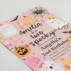 May include: Pink Halloween-themed invitation with the text "Amelia is a two spooky" and "Amelia's 2nd Birthday." The design includes illustrations of ghosts, pumpkins, bats, and a spiderweb. The invitation is for a birthday party.