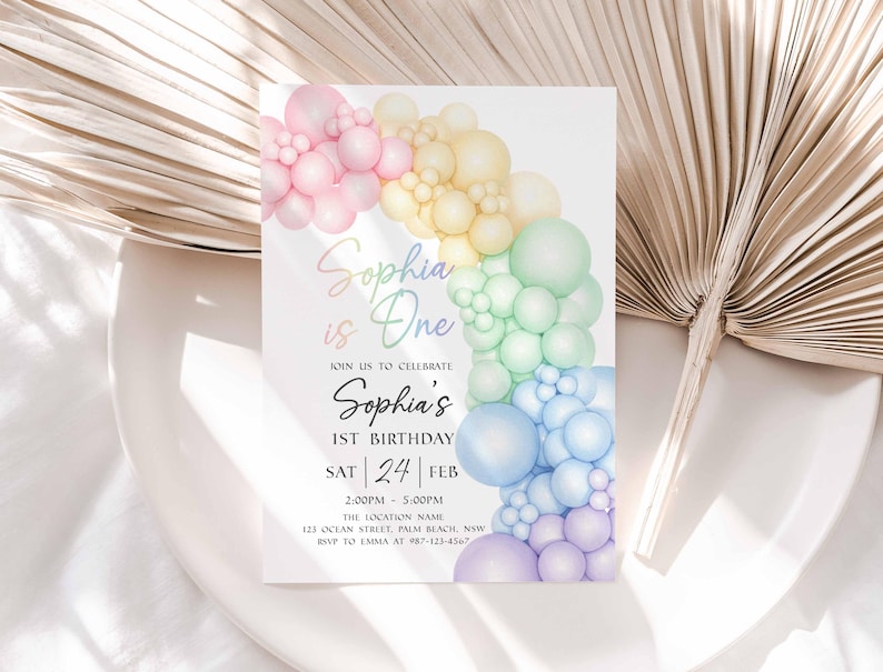 May include: A pastel rainbow-themed birthday invitation. The invitation features a colorful balloon arch and the text "Sophia is One." The date is Saturday, February 24th, with the time and location details below. The design is soft and whimsical.