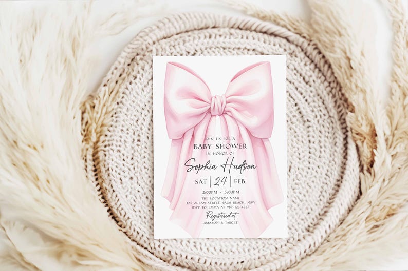 Op de afbeelding: Een uitnodiging voor een babyshower met een grote, zachte roze strik. De uitnodiging bevat de tekst "Doe mee voor een babyshower ter ere van Sophia Hudson" en evenementdetails. De achtergrond is een neutraal, getextureerd oppervlak.