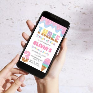 May include: A smartphone displays a colorful birthday party invitation. The invitation features the text "THREE Scoops of Fun" and "Olivia's Birthday Party." Decorative ice cream cones and sprinkles adorn the design. The date is Saturday, July 27, 2024.