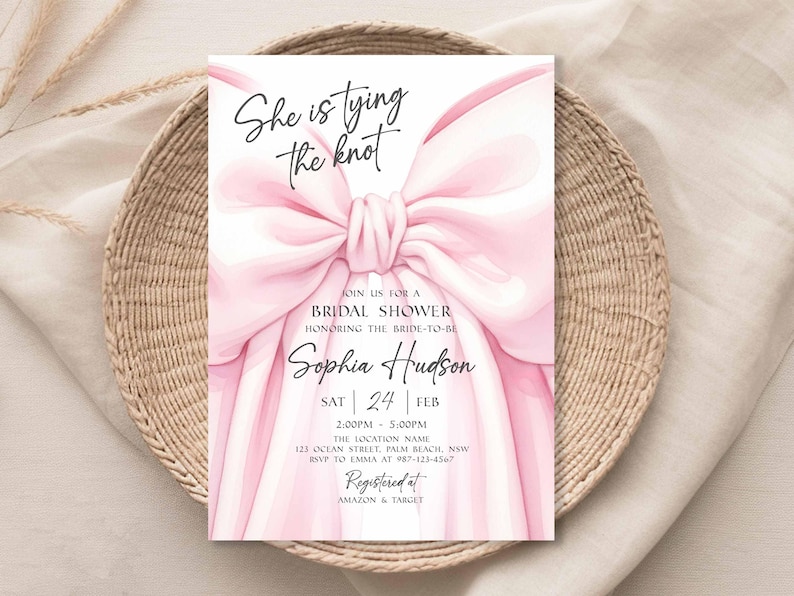 K&ouml;nnte beinhalten: Eine rosa Brautparty-Einladung mit dem Text "She is tying the knot" und dem Namen "Sophia Hudson". Die Einladung zeigt eine gro&szlig;e rosa Schleife und liegt auf einem geflochtenen Korb.