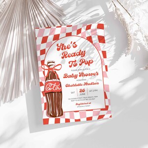May include: Baby shower invitation with a red and pink checkered background. The invitation features a vintage-style illustration of a cola bottle with a red bow. Text includes "She's Ready To Pop" and event details.