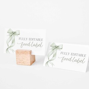 May include: Two white food label cards with a watercolor sage green bow and ribbon design. The text "FULLY EDITABLE food label" is printed on the cards. One card is propped up on a small wooden block.