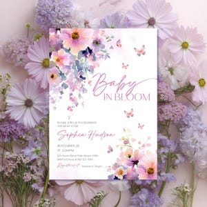 Może przedstawiać: Zaproszenie na baby shower z kwiatowym wzorem w odcieniach r&oacute;żu, fioletu i bieli. Tekst "Baby in Bloom" jest napisany elegancką czcionką. Zaproszenie zawiera r&oacute;wnież imię przyszłej mamy, datę, godzinę i miejsce.