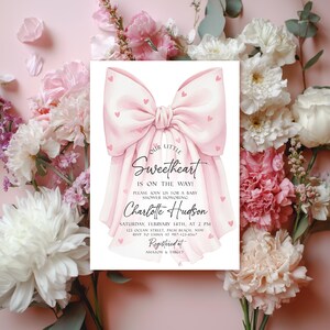 May include: A baby shower invitation featuring a large pink bow adorned with small hearts. The invitation text reads "Our Little Sweetheart is on the way!" and includes details for the event, such as the date, time, location, and honoree's name.