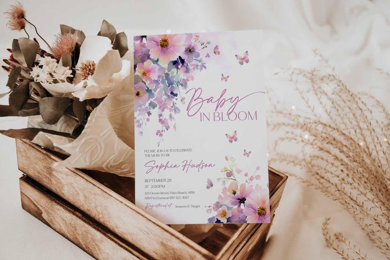 Może przedstawiać: Zaproszenie na baby shower z kwiatowym wzorem akwarelowym. Zaproszenie zawiera tekst "Baby in Bloom" i imię "Sophia Hudson". Zaproszenie jest ozdobione r&oacute;żowymi i fioletowymi kwiatami i motylami. Zaproszenie jest wyświetlane w drewnianej skrzyni.