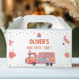 May include: A white favor box with a red fire truck, a fire hat, and a fire extinguisher. The box has a handle and says "Oliver's Birthday Party" on the front.