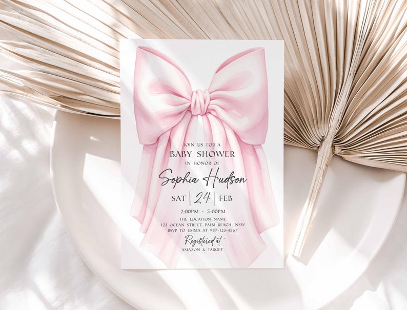 Op de afbeelding: Babyborrel uitnodiging met een grote, aquarel-stijl roze strik. De uitnodiging bevat de tekst "JOIN US FOR A BABY SHOWER IN HONOR OF Sophia Hudson" met evenementdetails en RSVP-informatie. Geregistreerd bij Amazon & Target.