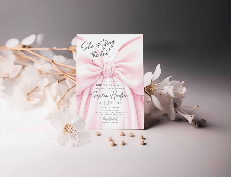 K&ouml;nnte beinhalten: Eine Einladung zur Brautparty mit einem rosa Aquarell-Schleifendesign. Die Einladung enth&auml;lt den Text "She is tying the knot" und Details zur Veranstaltung. Wei&szlig;e Blumen und kleine Perlen befinden sich im Vordergrund.