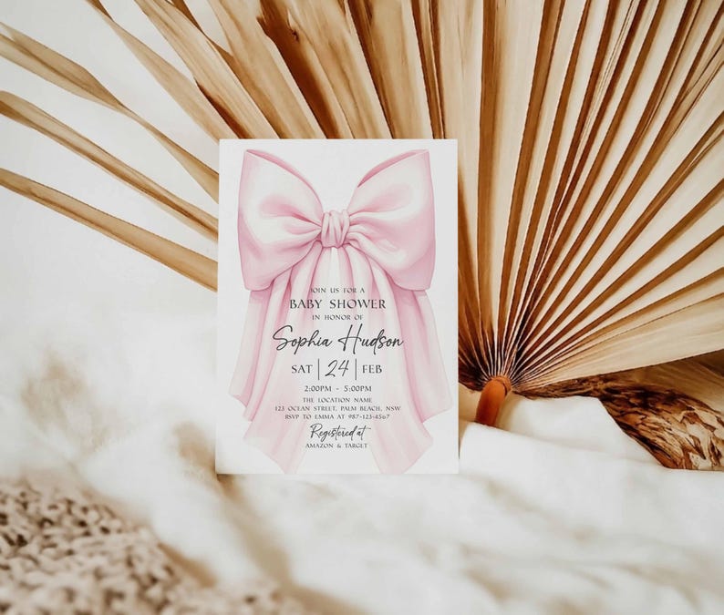Op de afbeelding: Een uitnodiging voor een babyshower met een grote roze strik. De uitnodigingstekst bevat de woorden "Ann us for a Baby Shower in Honor of Sophia Hudson", samen met de datum en tijd. De achtergrond toont gedroogde palmbladeren.