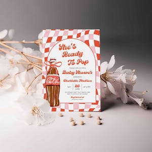 May include: Baby shower invitation with a retro design. The invitation features a Coca-Cola bottle illustration and the text "She's Ready To Pop." The background has a red and pink checkered pattern. The invitation includes the honoree's name, date, and time.