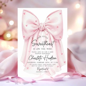 May include: A baby shower invitation featuring a large pink bow adorned with small pink hearts. The invitation reads "Our Little Sweetheart is on the way!" and includes details for Charlotte Hudson's baby shower, including date, time, and location.