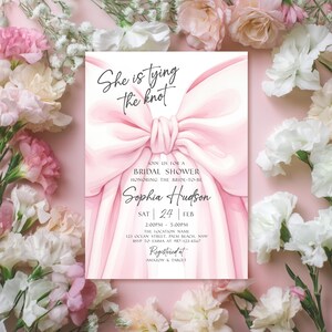 K&ouml;nnte beinhalten: Eine rosa Brautparty-Einladung mit einer gro&szlig;en Schleifenillustration und dem Text "She is tying the knot". Die Einladung enth&auml;lt Details f&uuml;r Sophia Hudsons Brautparty, einschlie&szlig;lich Datum, Uhrzeit und Ort. Die Einladung ist von rosa und wei&szlig;en Blumen umgeben.