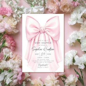Op de afbeelding: Een babyborrel uitnodiging met een roze strik. De uitnodiging bevat de tekst "Doe met ons mee voor een babyshower ter ere van Sophia Hudson" met datum, tijd en locatie. Omringd door roze en witte bloemen.