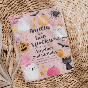 May include: A pink Halloween-themed invitation with the text "Amelia is a two spookyne" and details for a 2nd birthday party. The design includes ghosts, pumpkins, bats, and a black cat with a bow.
