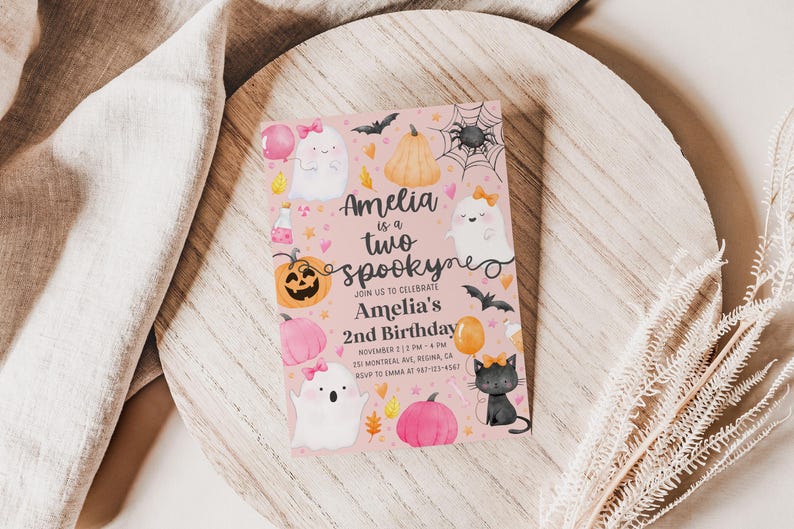 May include: A pink Halloween-themed invitation with the text "Amelia is a two spooky" and details for a second birthday celebration. The design includes ghosts, pumpkins, bats, and a black cat.