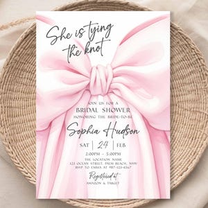 K&ouml;nnte beinhalten: Eine rosa Brautparty-Einladung mit einer gro&szlig;en Schleife. Die Einladung enth&auml;lt den Text "She is tying the knot" sowie Details zur Veranstaltung, einschlie&szlig;lich des Namens der Braut, Datum, Uhrzeit und Ort. Die Einladung ist bei Amazon & Target registriert.