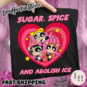 May include: Black tote bag with a Powerpuff Girls design. The image shows the characters inside a pink heart, with the text "SUGAR, SPICE AND ABOLISH ICE" in pink. Yellow stars are also included in the design.